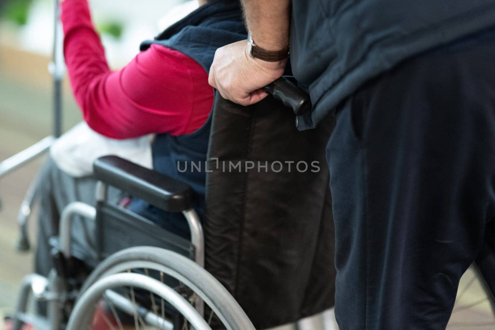 Partial view of a person assisting someone in a wheelchair, showing hands and wheels.