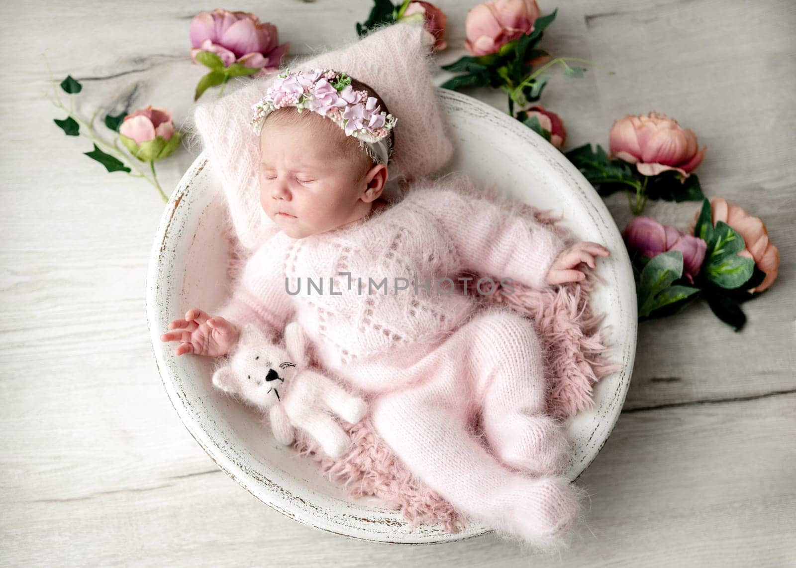 Newborn Baby Girl In Wooden Bowl With Flowers Around During Studio Photoshoot