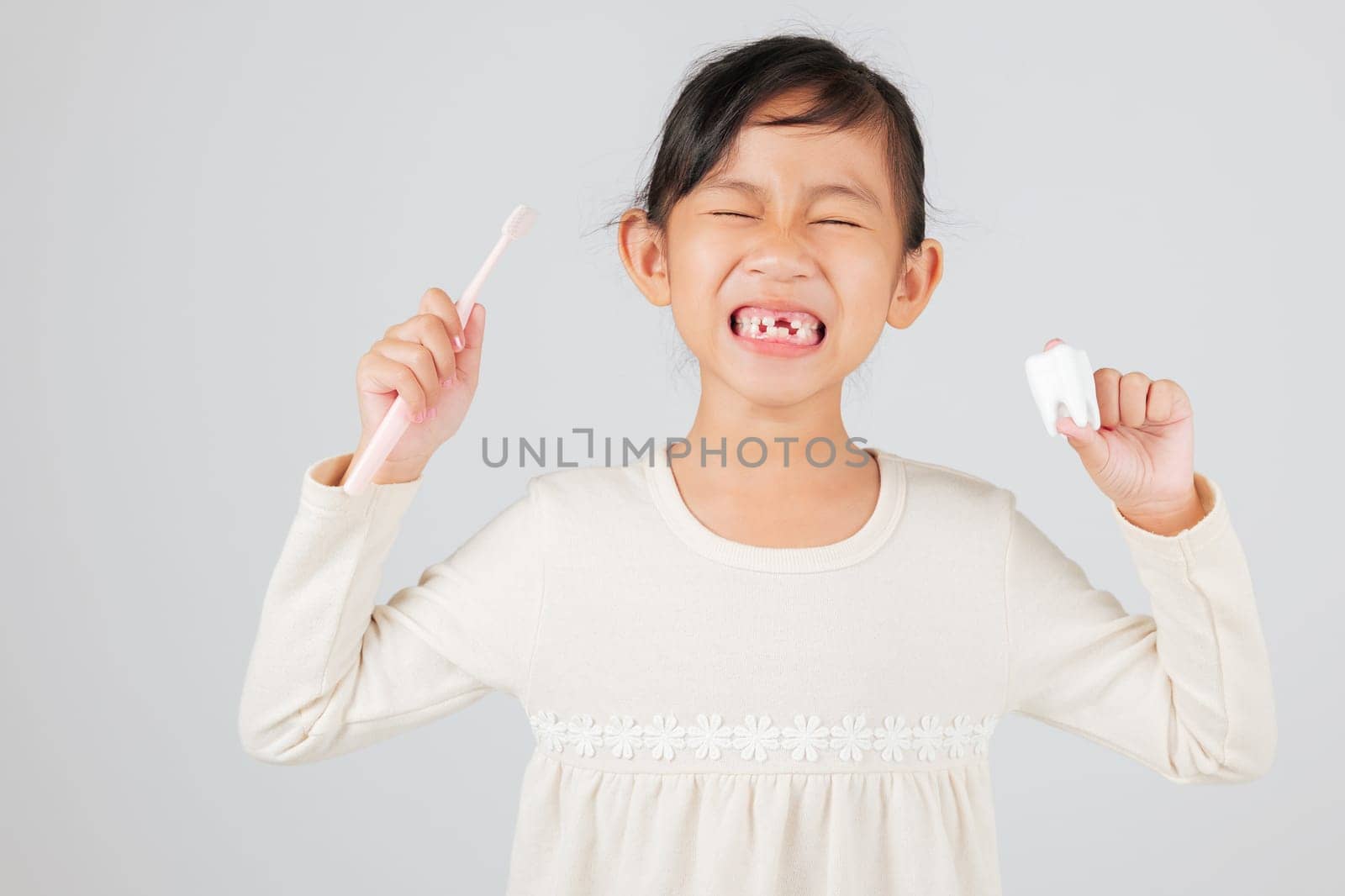 Kid girl holds toothbrush and tooth model, dentist explains tooth loss. Asian child smiles, showing missing milk teeth and gap, promoting dental hygiene habits. isolated white background