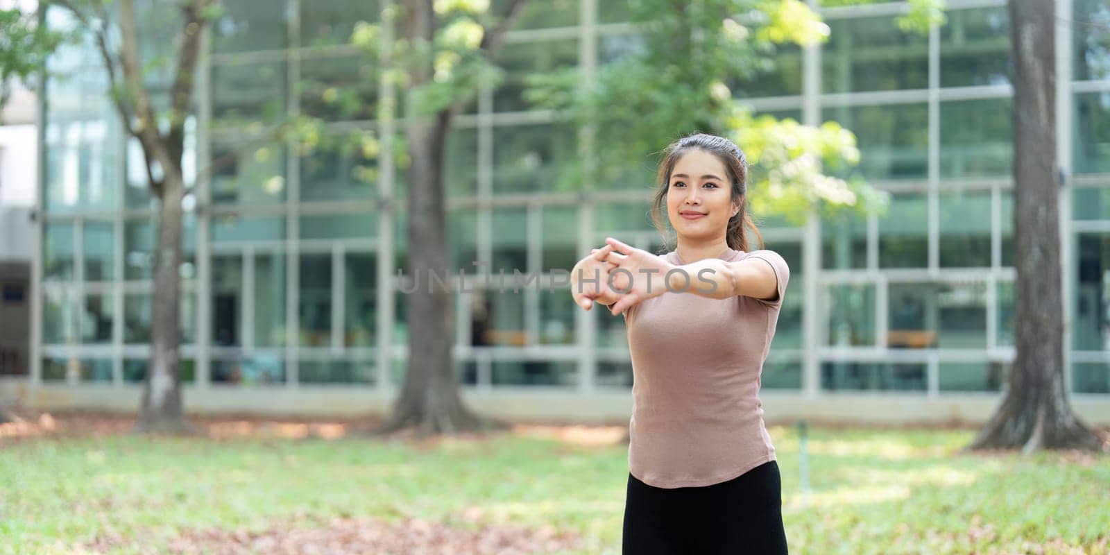 A woman performs arm stretches in a green park, promoting wellness and fitness through outdoor activity.