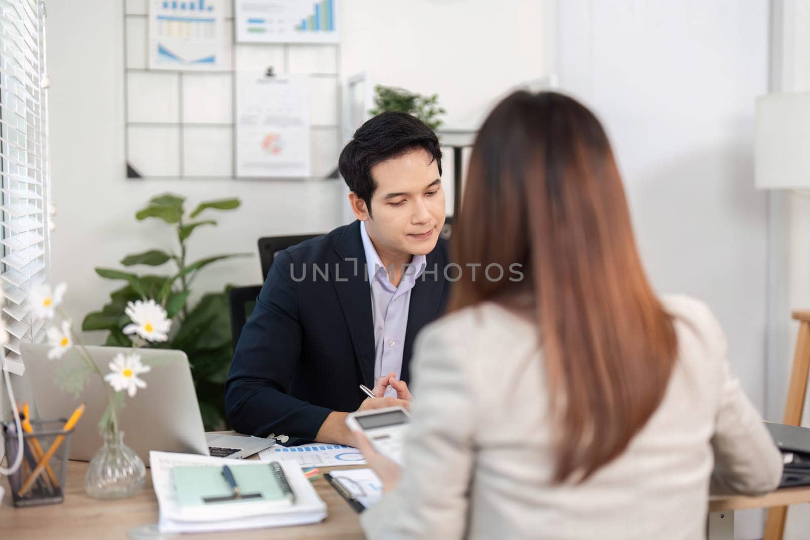 A businessman attentively listening to a female colleague while discussing financial strategies in a bright office environment.