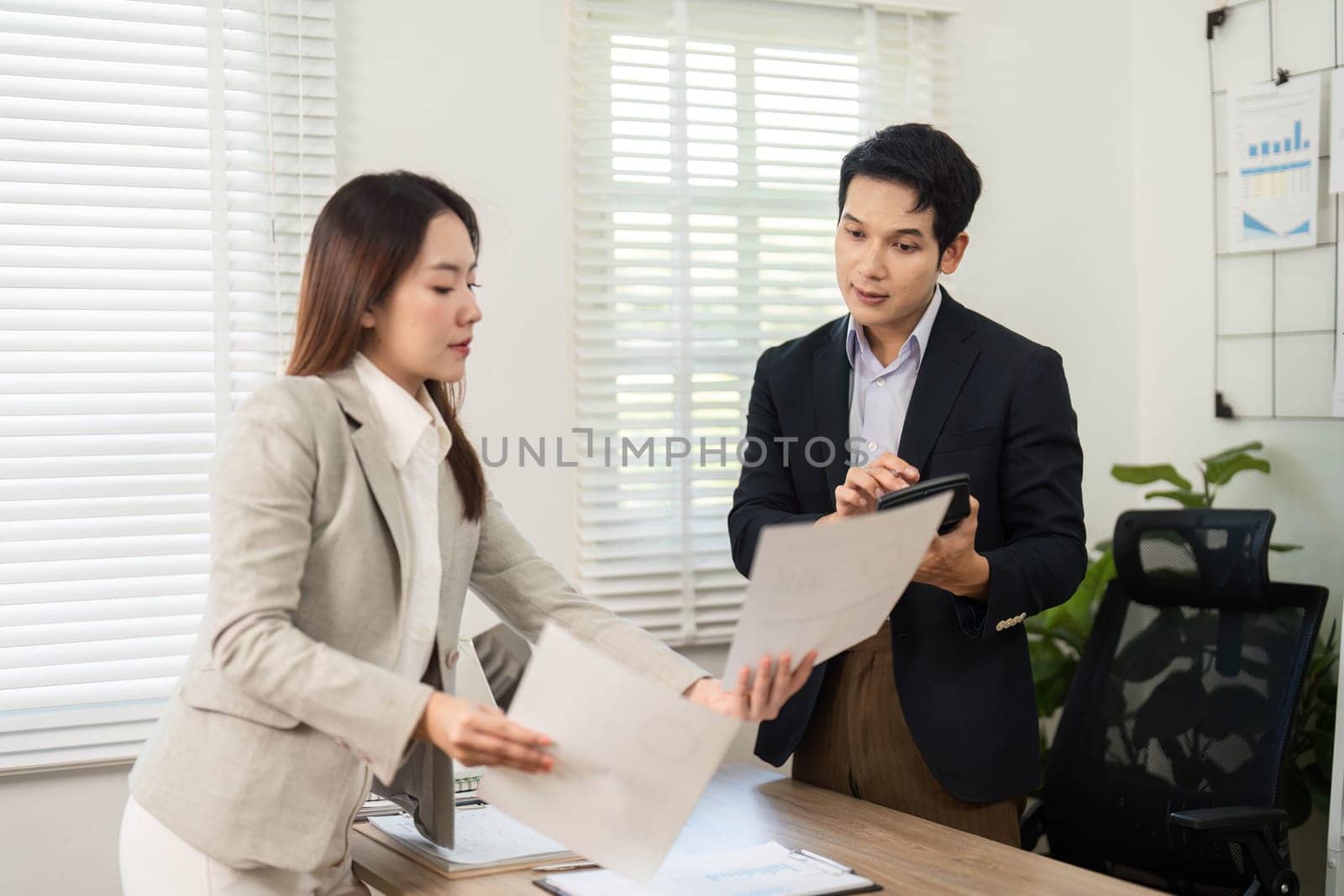 A woman presents documents to a man while discussing project details, highlighting teamwork and professionalism in a corporate setting.