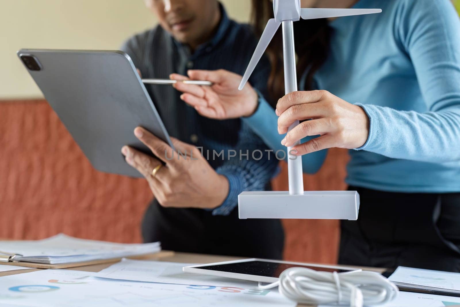 Two colleagues engage in a discussion about renewable energy, using a wind turbine model and digital tools for effective collaboration.