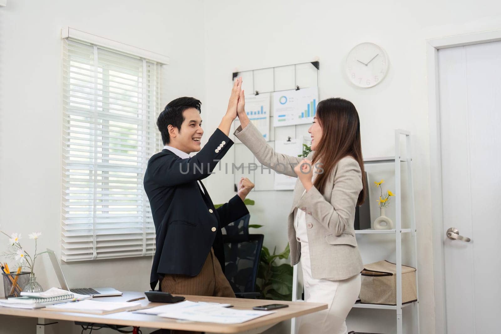 Two professionals celebrating their success with a high five in a contemporary office setting, embodying teamwork and positivity.