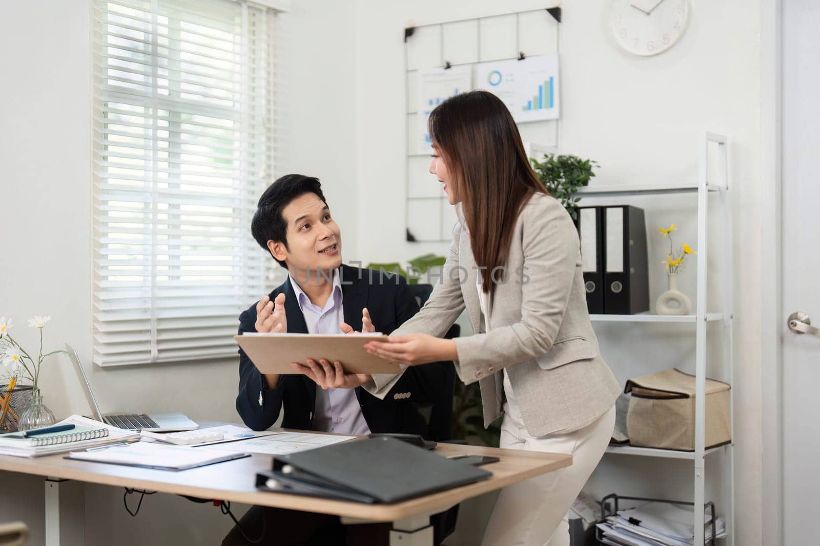 Two colleagues engage in a productive discussion about financial reports, showcasing teamwork and collaboration in a bright office environment.