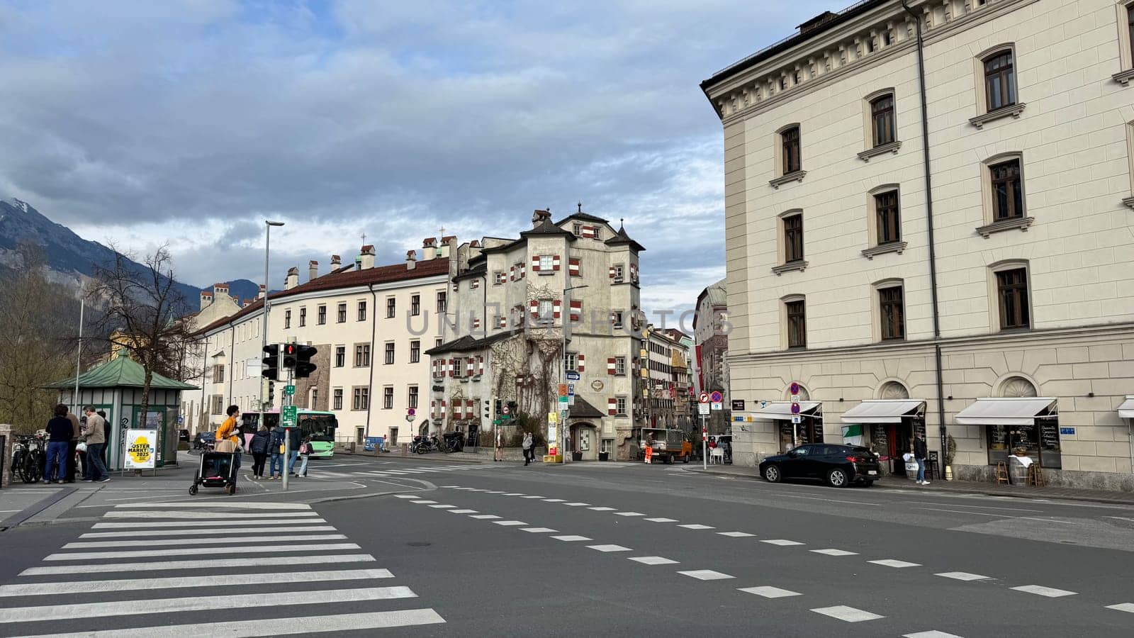 Innsbruck, Austria - March 28, 2025: Historic buildings at urban busy street in Innsbruck with people, historic architecture, pedestrians crossing and vehicles, display architectural charm, vibrant urban life and a scenic street view with cars, bus