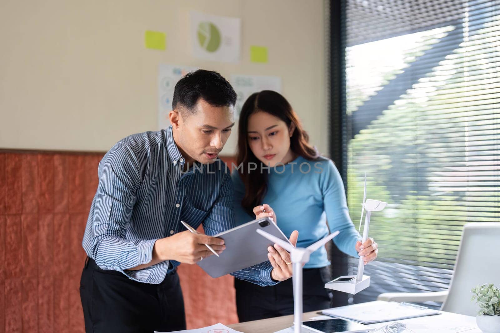 A team discusses renewable energy solutions, analyzing a wind turbine model and digital data on tablets in a modern workspace.