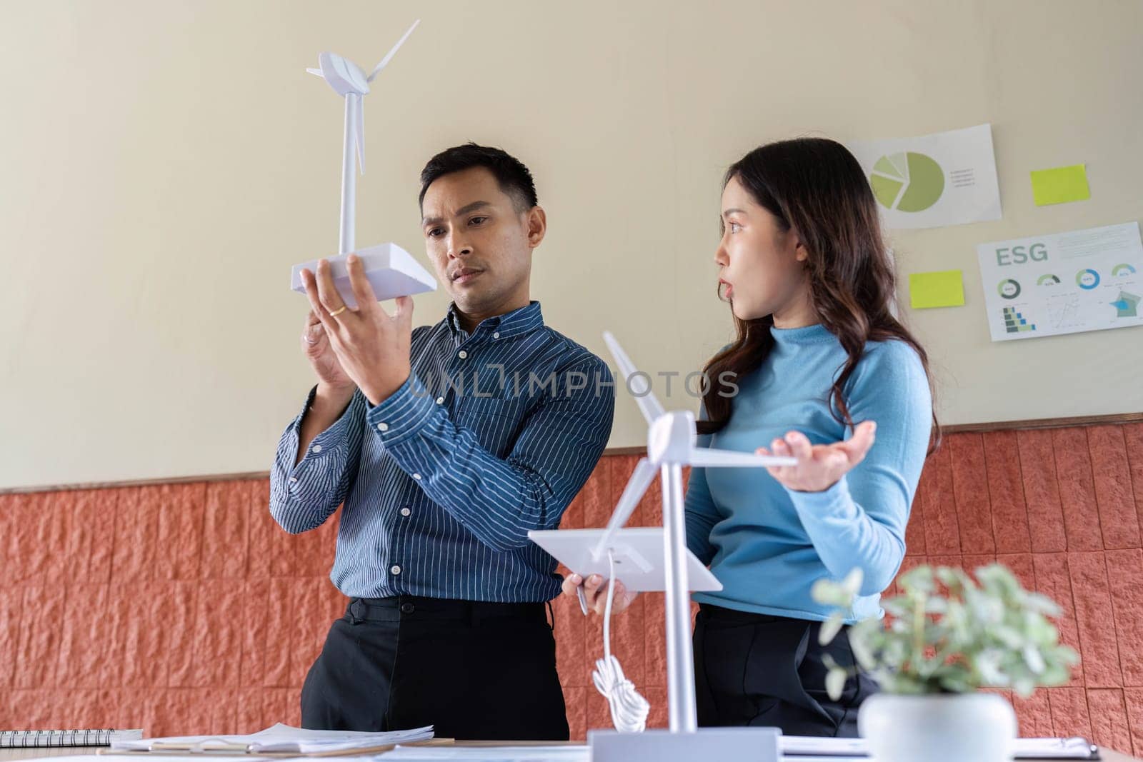 A female engineer discusses a wind turbine model with a male colleague, focusing on renewable energy solutions.