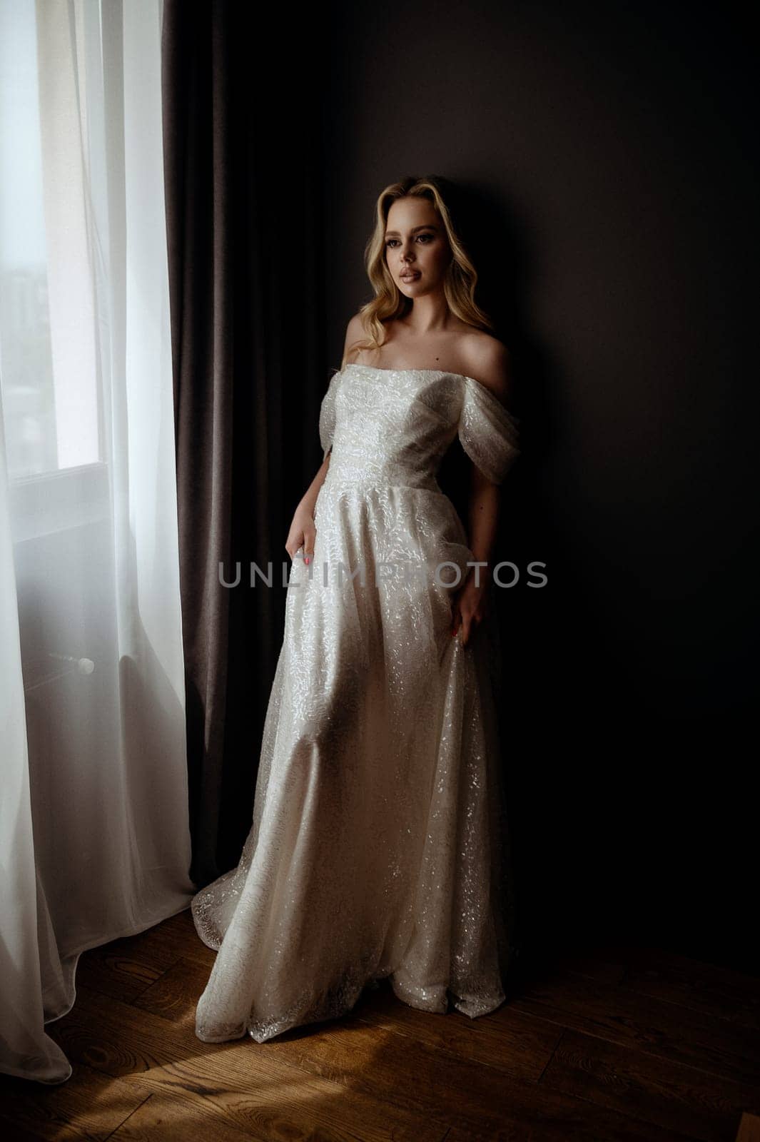Elegant bridal gown showcased in a minimalist setting with a model in a chic pose during an indoor shoot. A graceful bride poses in a long, white wedding dress. High quality photo