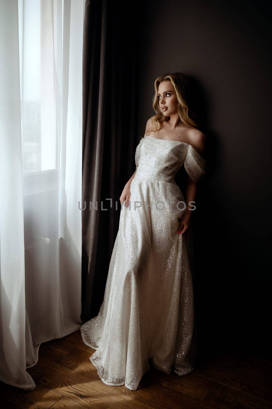 Elegant bridal gown showcased in a minimalist setting with a model in a chic pose during an indoor shoot. A graceful bride poses with elegance in a white wedding gown