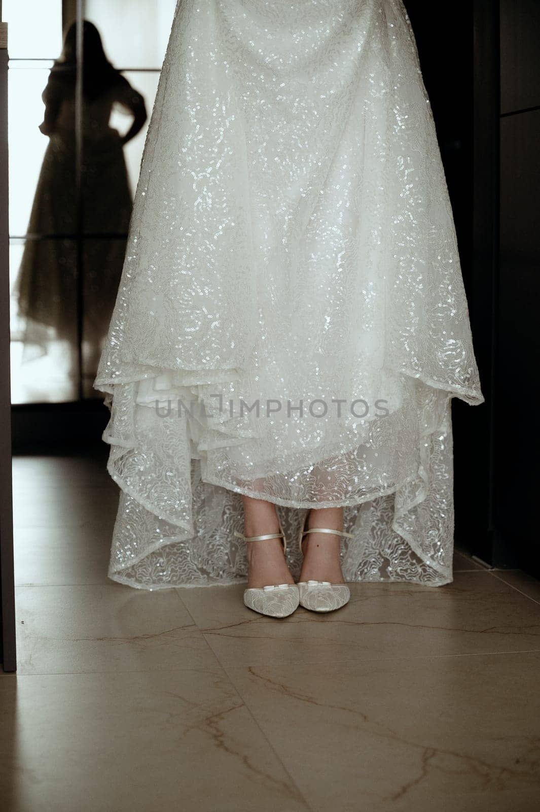 Close up of white lace wedding shoes. Bride shows shoes by lifting up skirt of wedding dress.