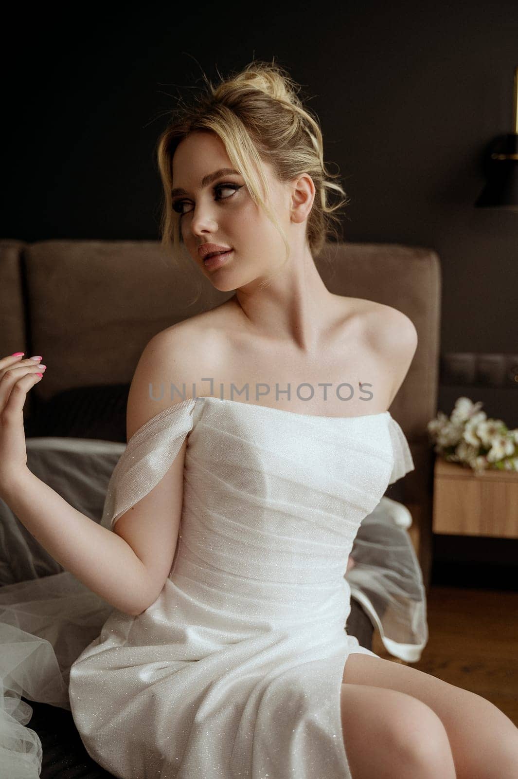 Beautiful bride Fashion portrait in wedding luxury dress with lace and crystals in dark interior. Blonde happy woman wears wedding white dress with wedding makeup and hairstyle.