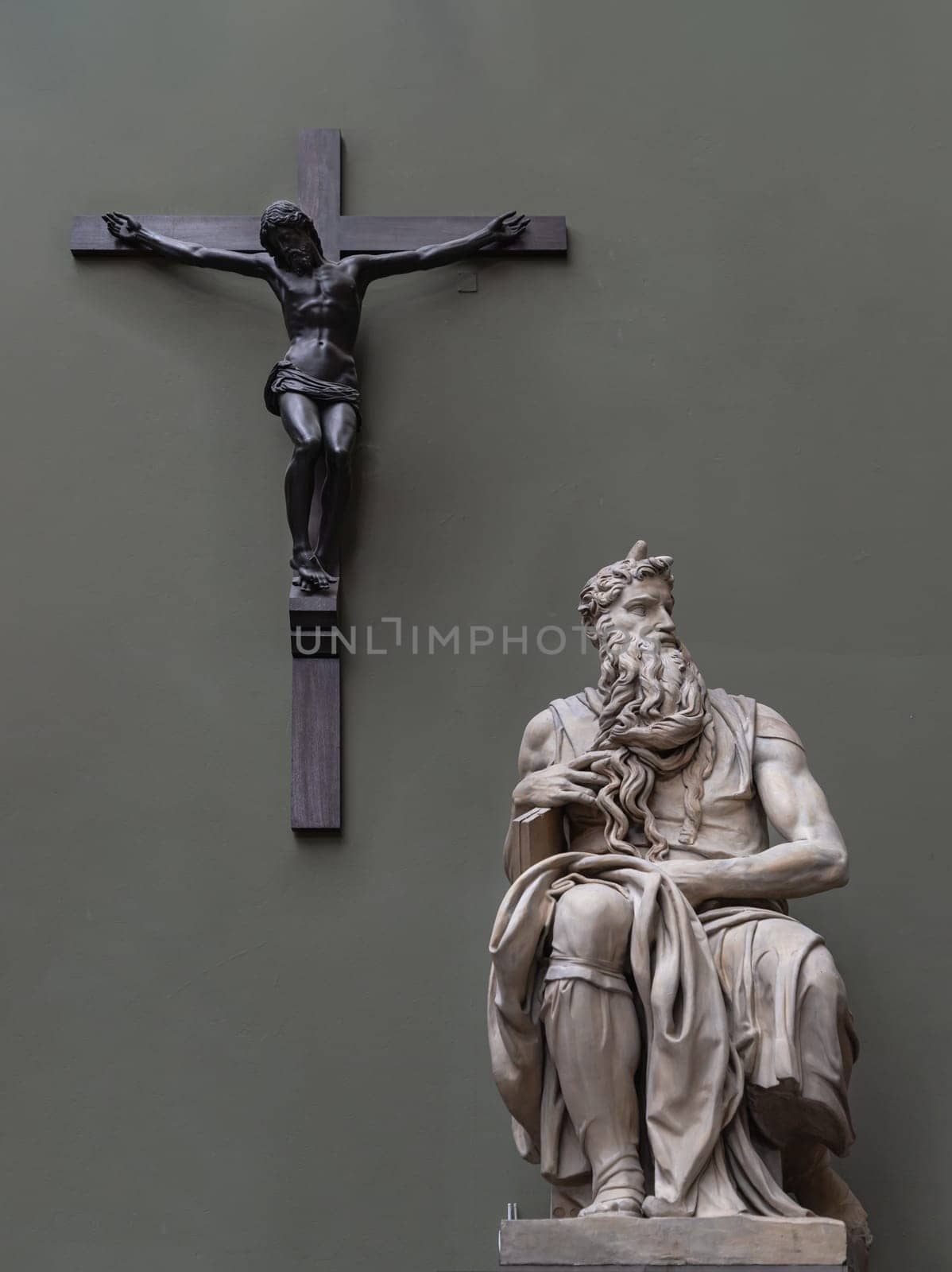 London, UK - May 07, 2025 - Marble statue of Moses by Michelangelo with The striking figure of Jesus Christ crucified on the Cross in the green wall background. The Moses is a sculpture by the Italian Renaissance artist Michelangelo Buonarroti, Displayed in The V&A (Victoria and Albert Museum) in London, use it as your Wallpaper, Poster and Space for text, Selective focus.