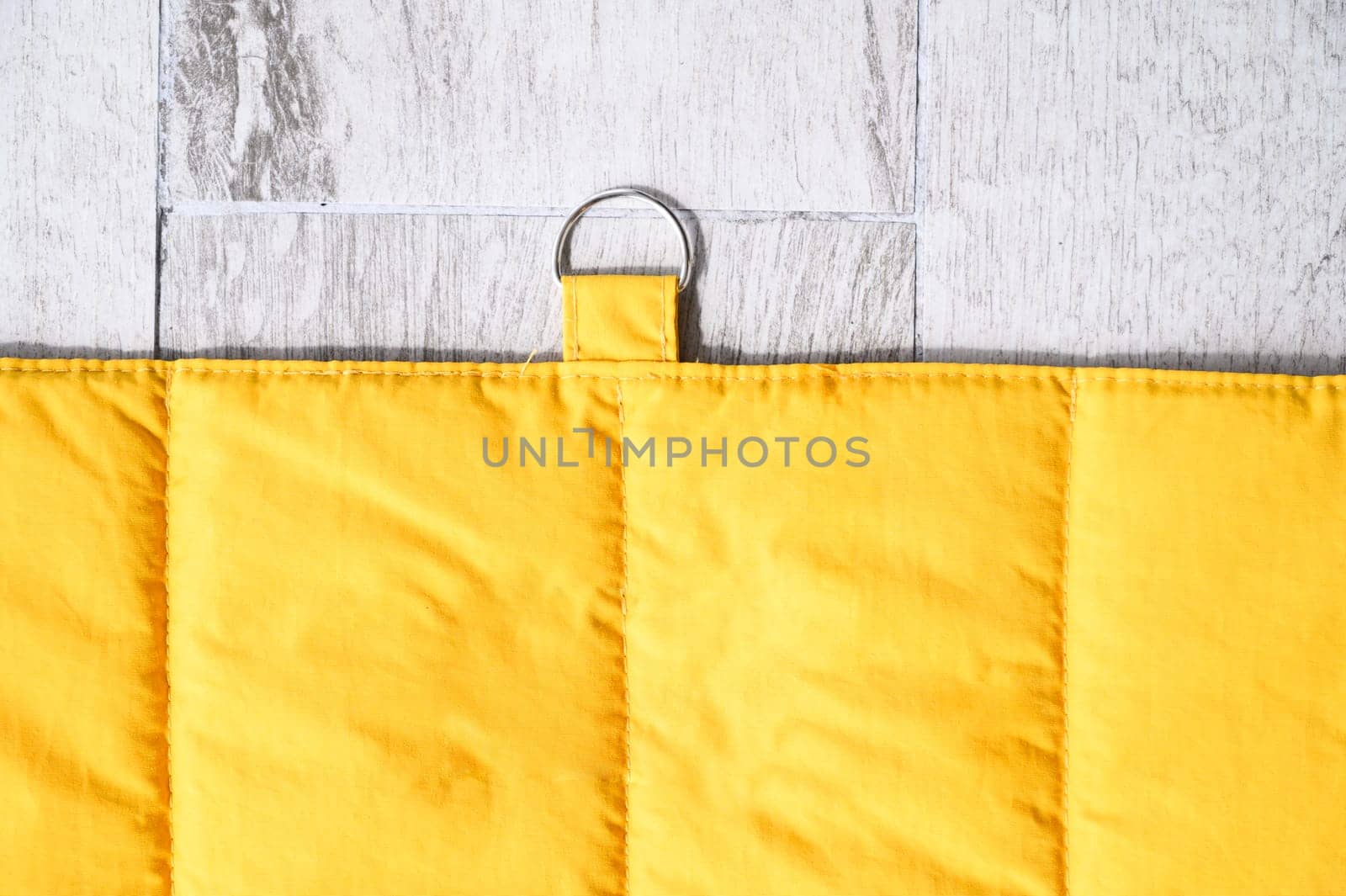 Yellow quilted pet blanket with metal ring hanging on light wooden wall, creating cozy and welcoming space for pets
