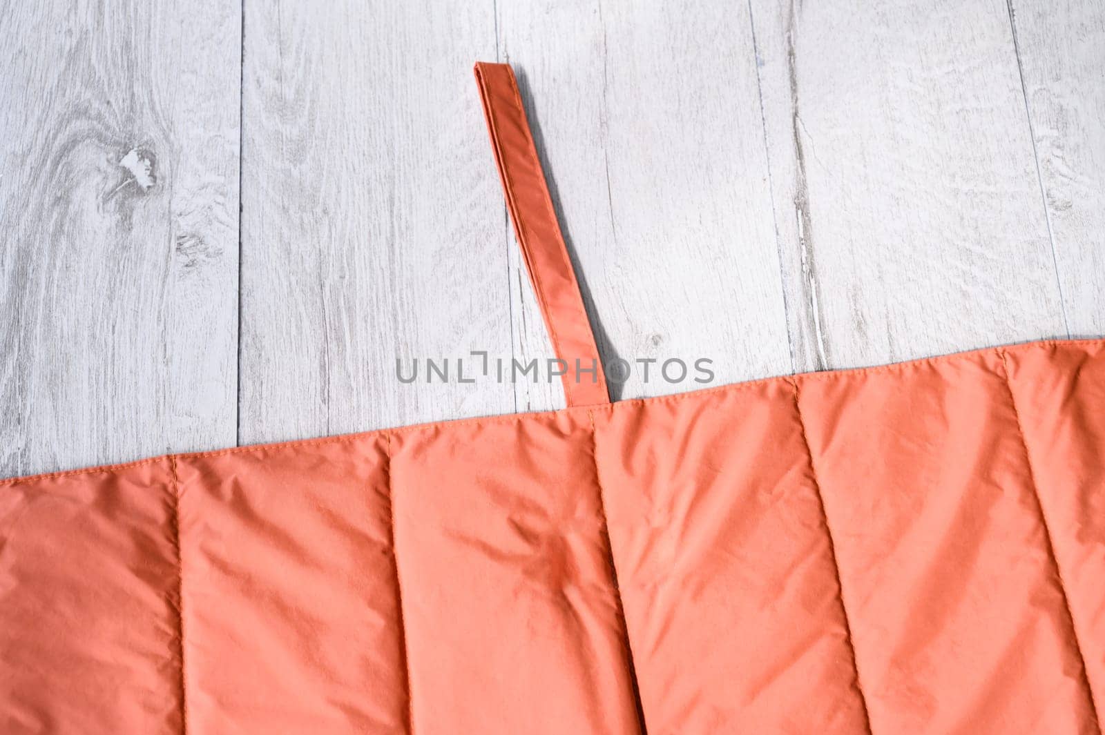 Orange waterproof and padded blanket or mat for pets like dogs and cats, folded on white wooden floor
