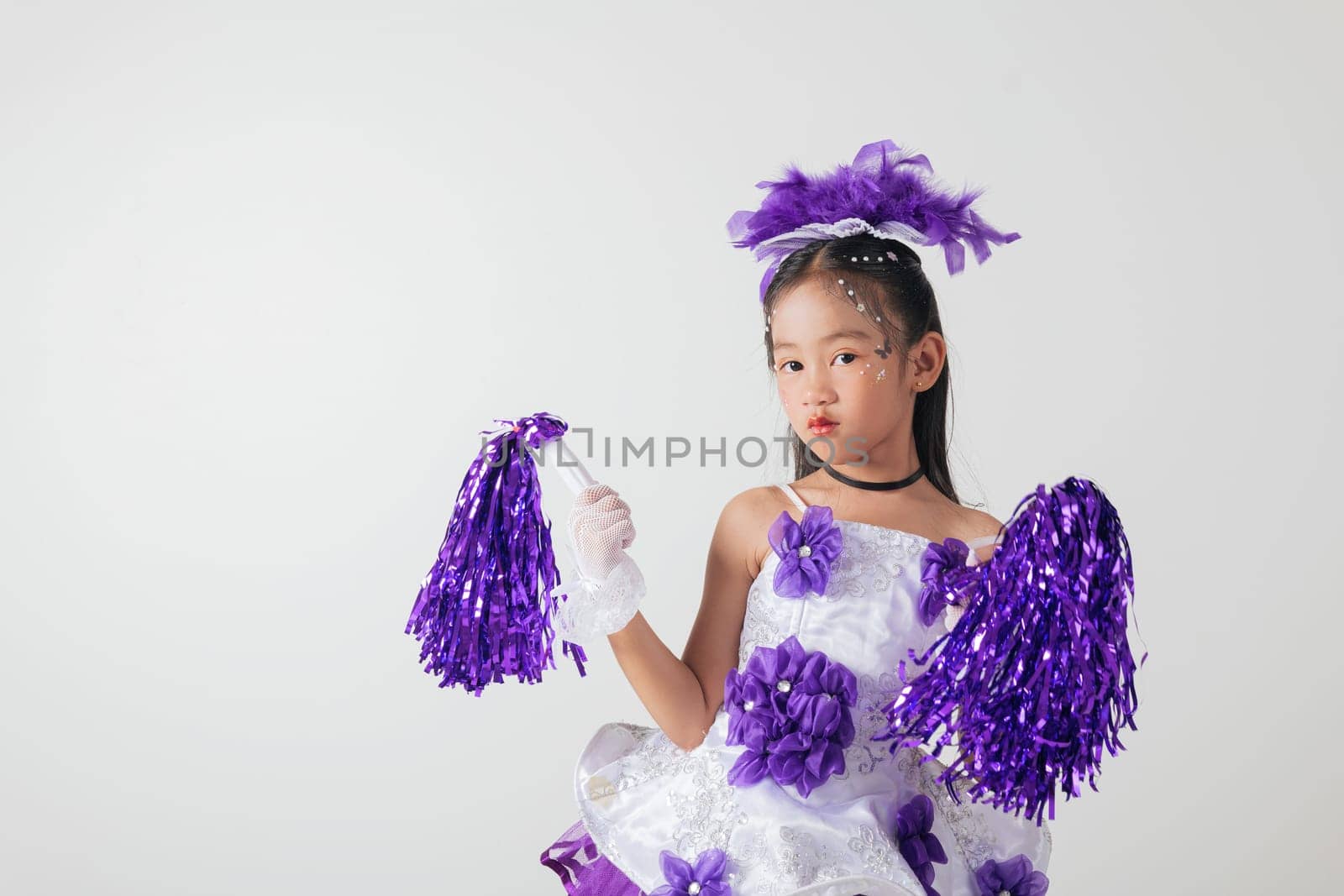 Smiling cheerleader girl wearing purple and white outfit with pom-poms. Studio portrait exuding energy and joy against a white background. cheerleader kid