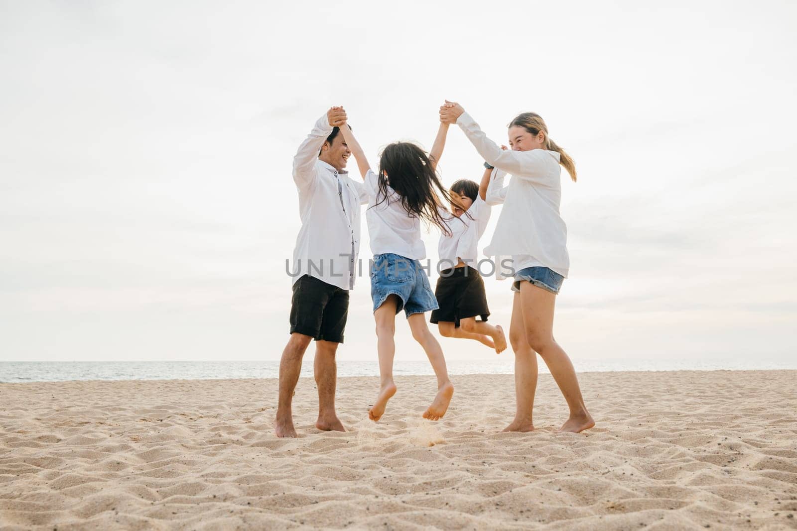 Beachside jubilation as an Asian family with father and mother holding children jumps into air. beautiful ocean serves as stunning backdrop highlighting family's happiness and playful bond.