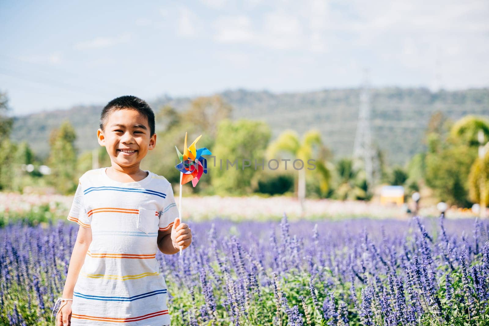 Little boy's portrait amid a flower garden joyfully holding a toy pinwheel. Springtime happiness and flying pinwheel signify fun in nature's sunny embrace evoking childhood joy.