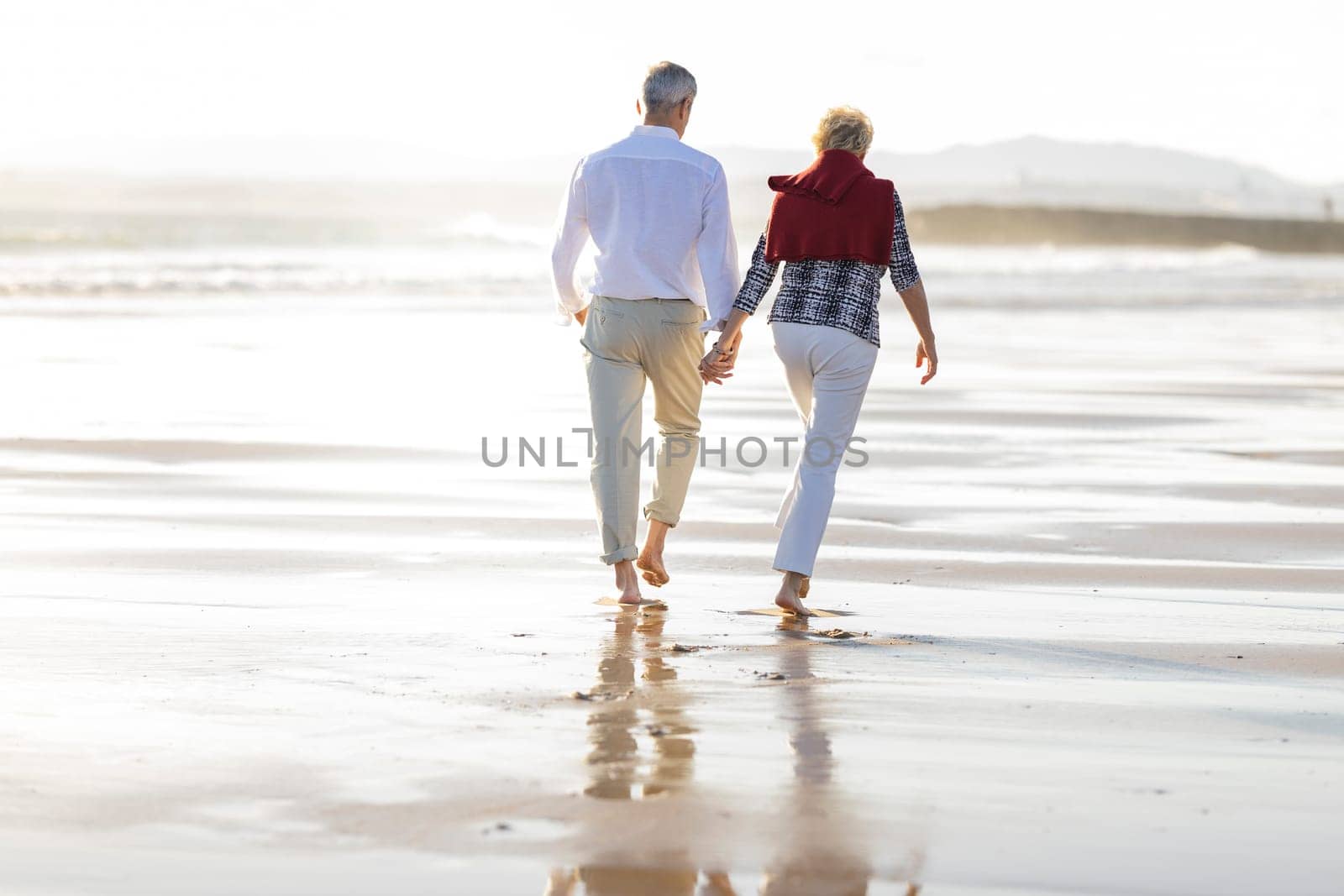 Retired couple enjoying walking on the beach at sunset, holding hands