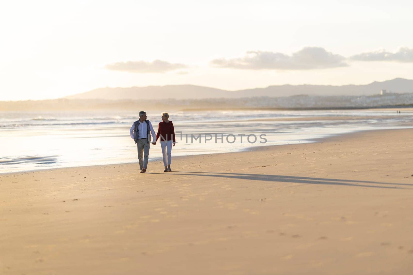 Elderly couple enjoying a romantic walk on the beach at sunset