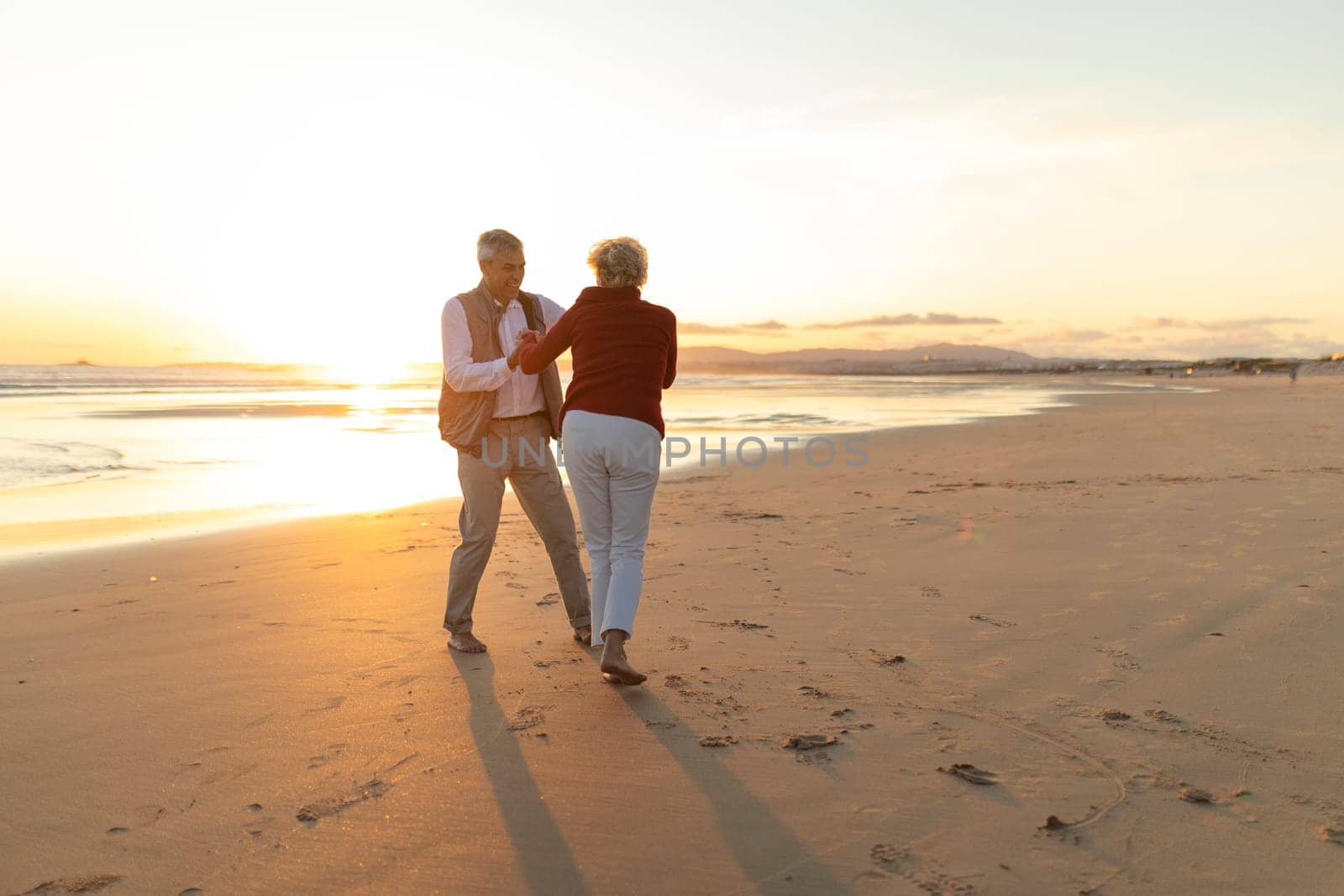 Elderly couple enjoying a romantic moment, dancing on the beach at sunset