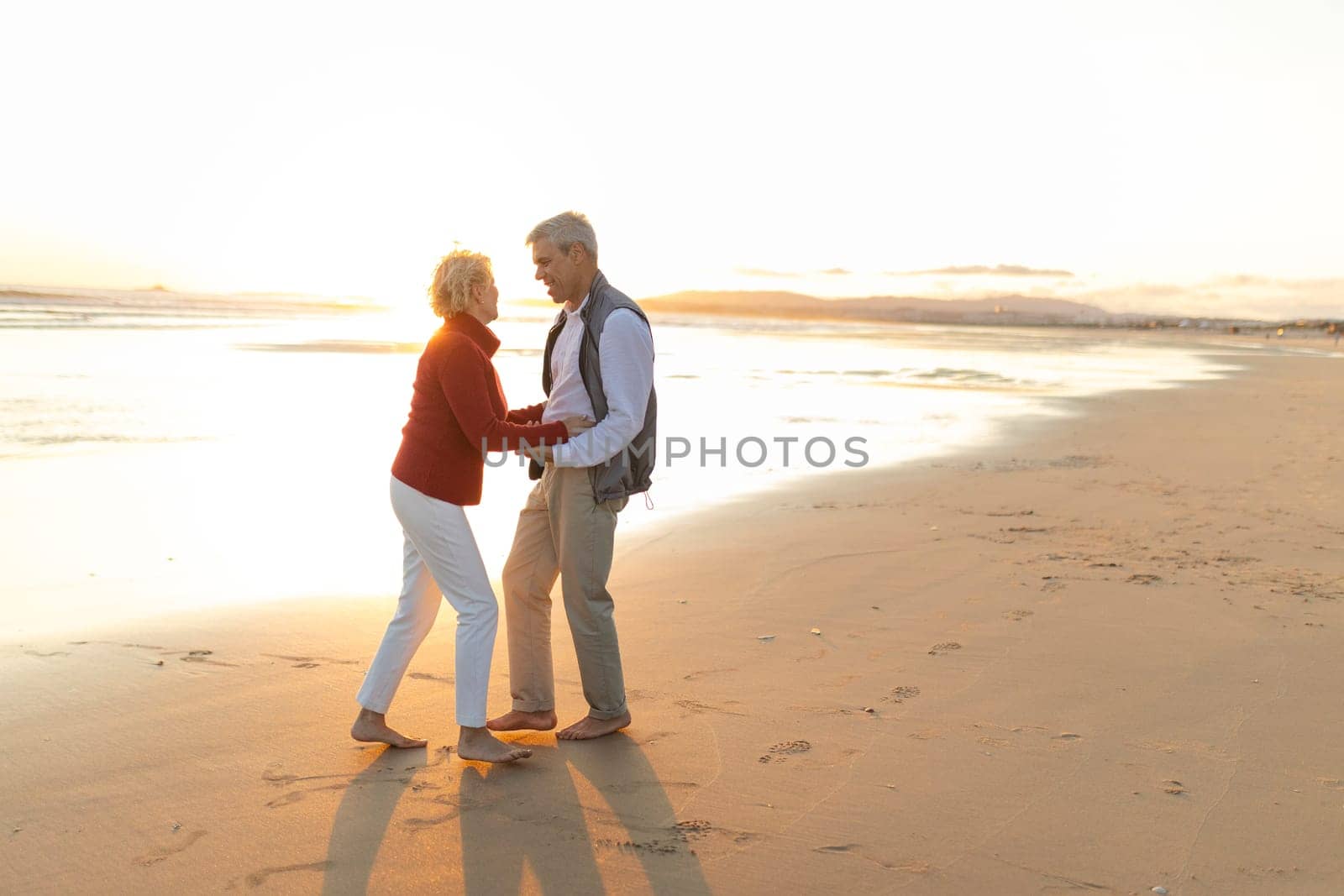 Elderly couple enjoying a romantic moment, dancing together on the beach during a beautiful sunset