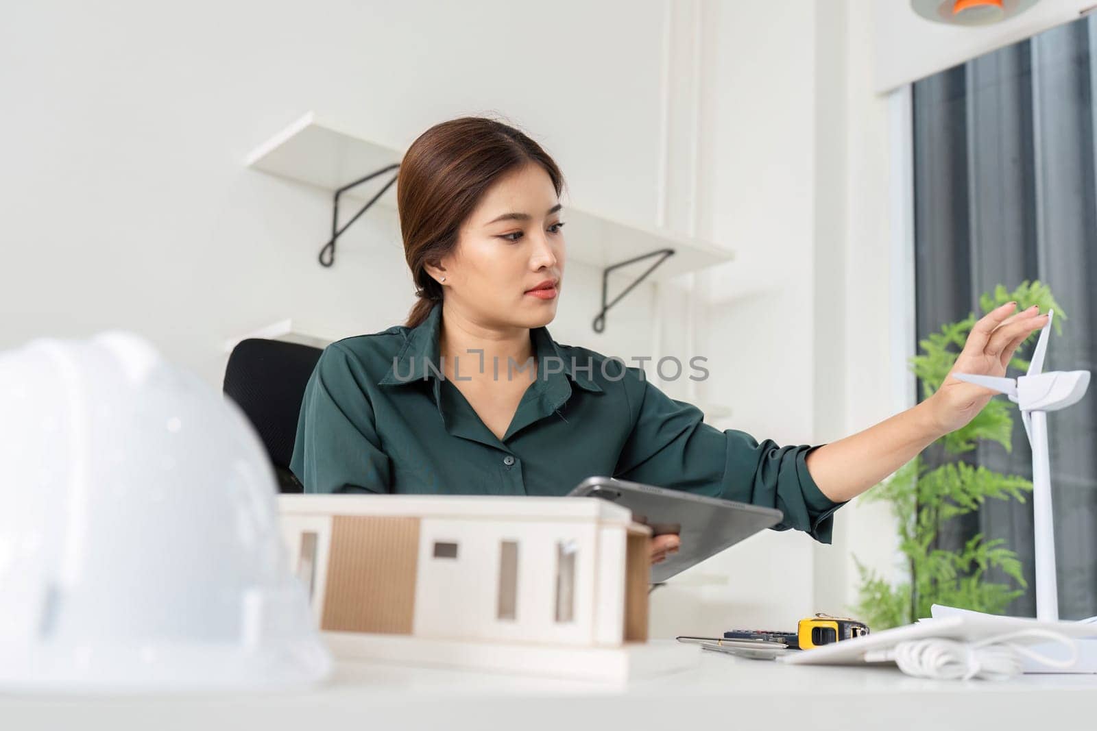 A woman architect inspects a sustainable model while using a tablet to enhance project accuracy in a bright office.