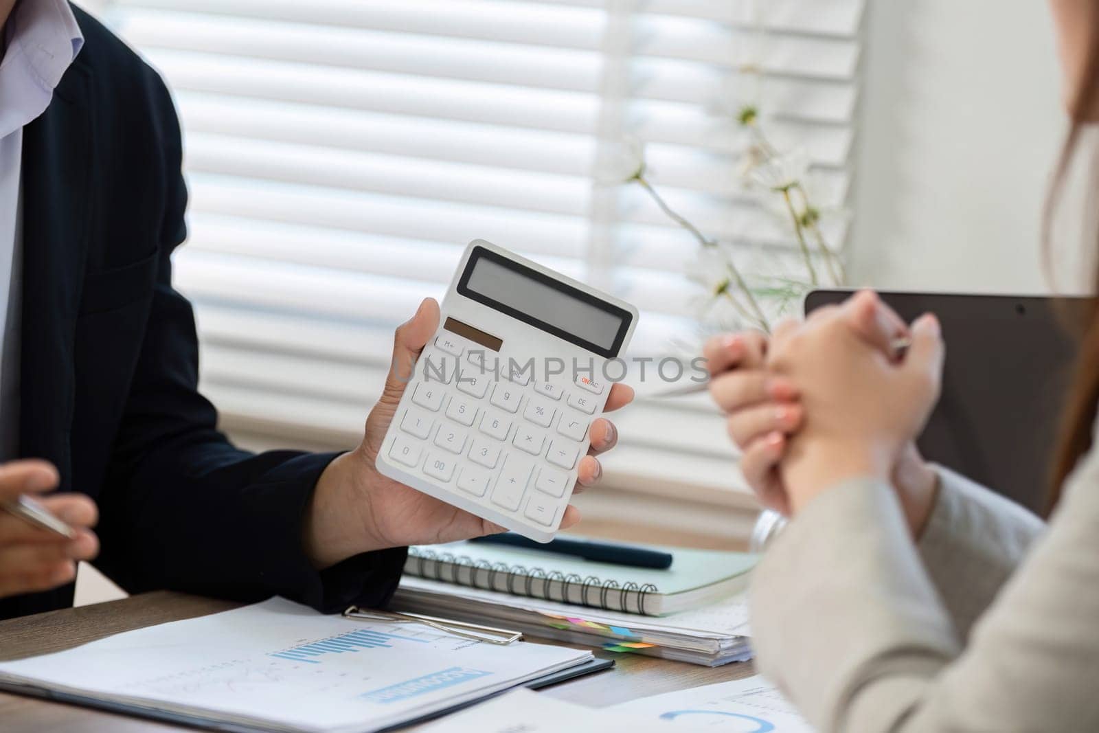 A businessman shows a calculator to a client during a financial consultation, emphasizing important data analysis in a modern office.