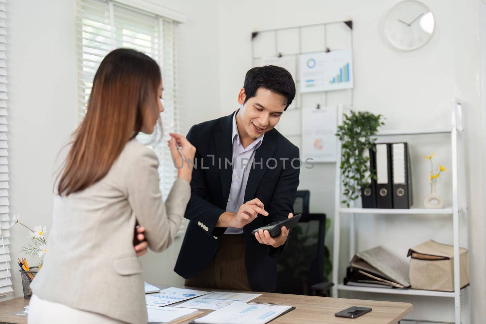 A businesswoman and businessman review project data on a tablet, emphasizing teamwork and technology in a modern office setting.