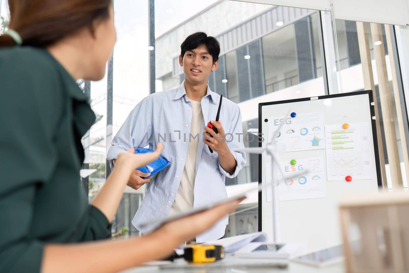 A young architect engages with a colleague in a modern office, discussing ESG strategies and sustainable practices.