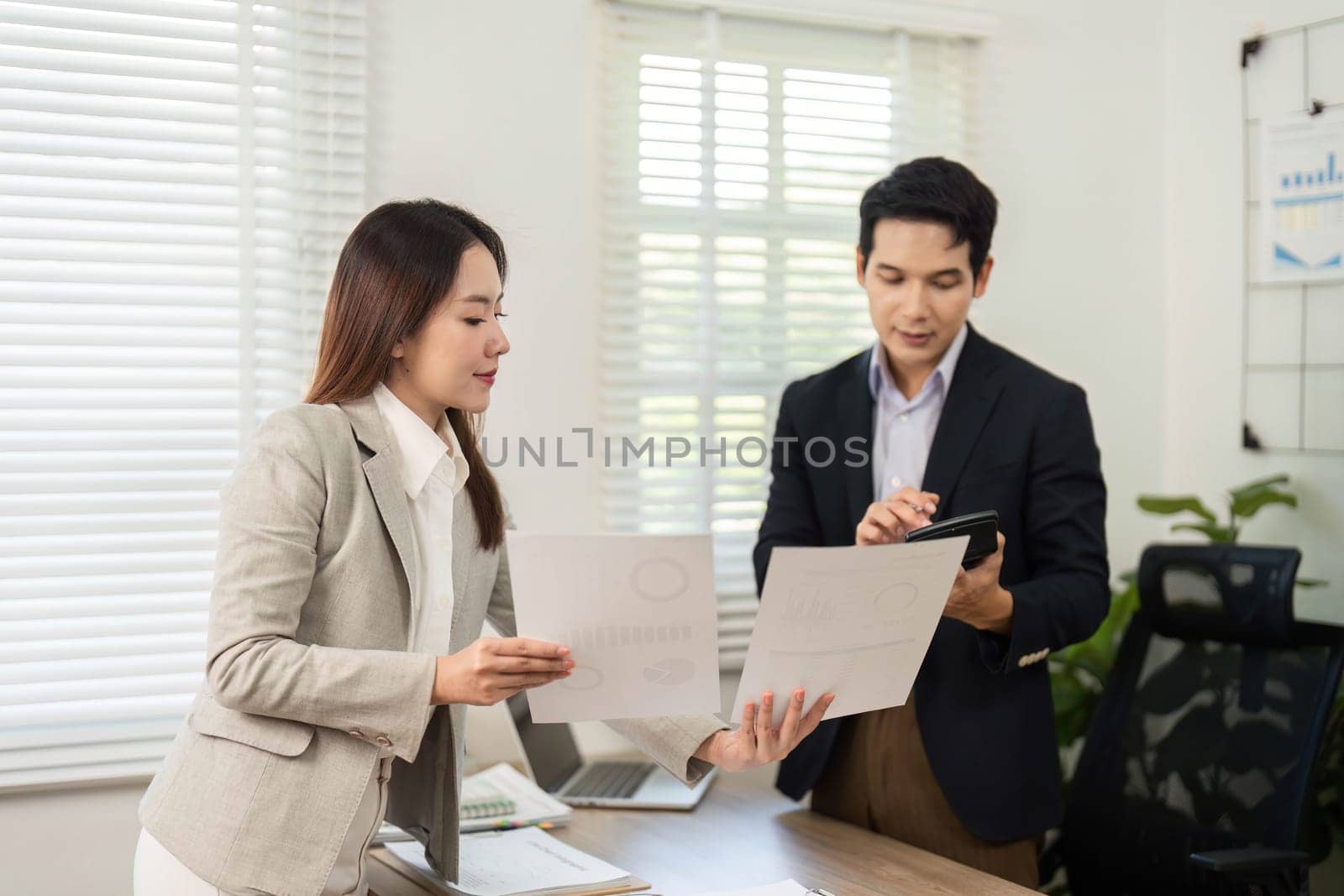 Two business professionals engage in a strategic discussion, reviewing project documents and collaborating in a contemporary office environment.