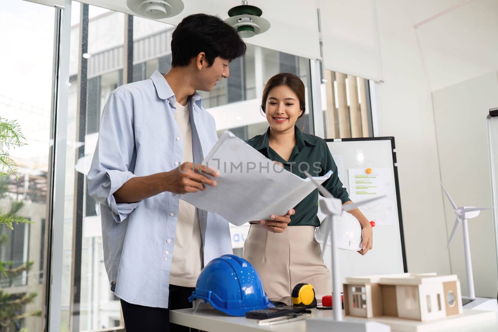 Two engineers reviewing blueprints and celebrating teamwork in a contemporary workspace. Concept of innovation and collaboration.