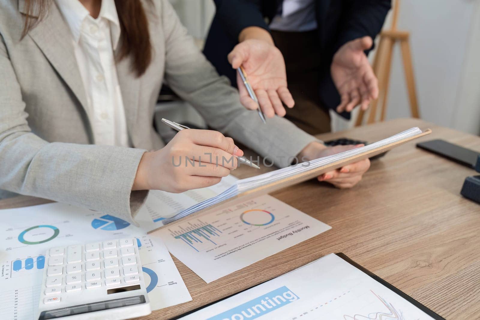 A business professional analyzing financial reports and charts while discussing strategies with a colleague in an office.