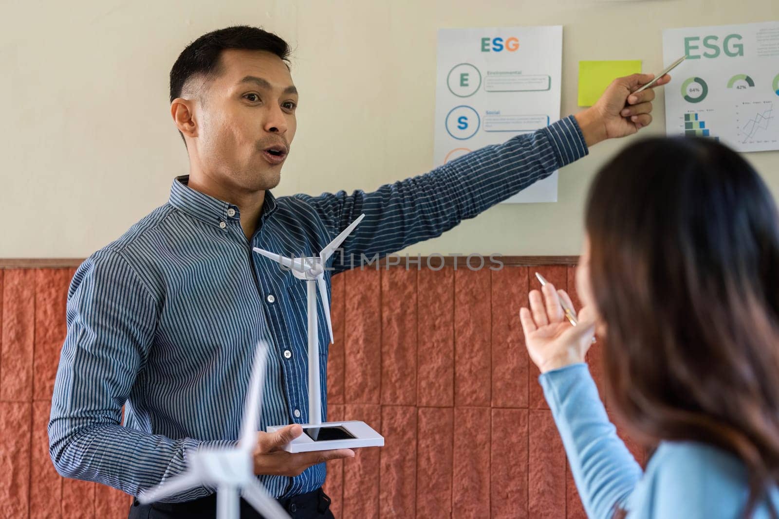 A man passionately presents wind turbine concepts to a woman, highlighting ESG principles in renewable energy.