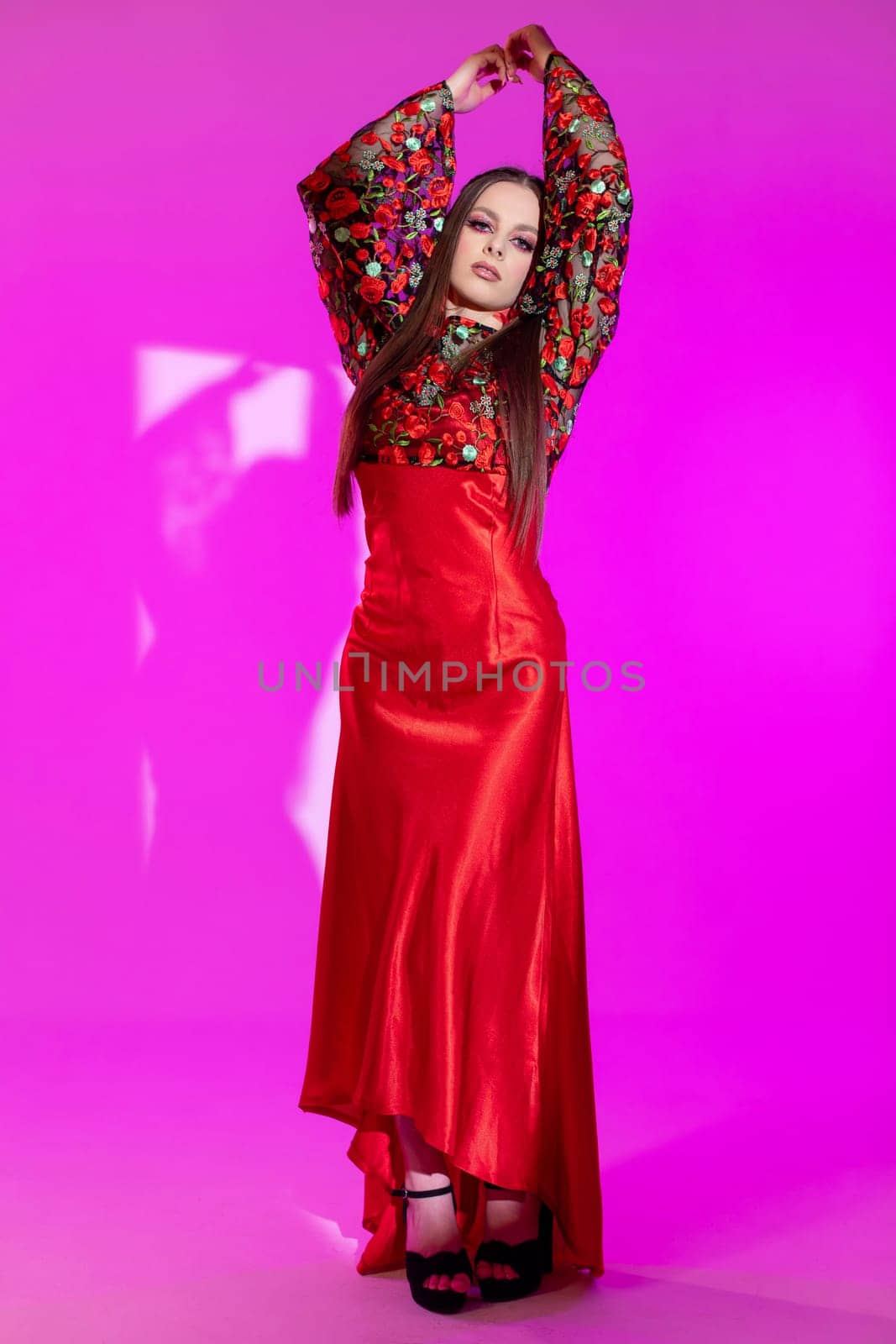 A striking model showcases a stylish red dress with unique embellishments against a vivid background.
