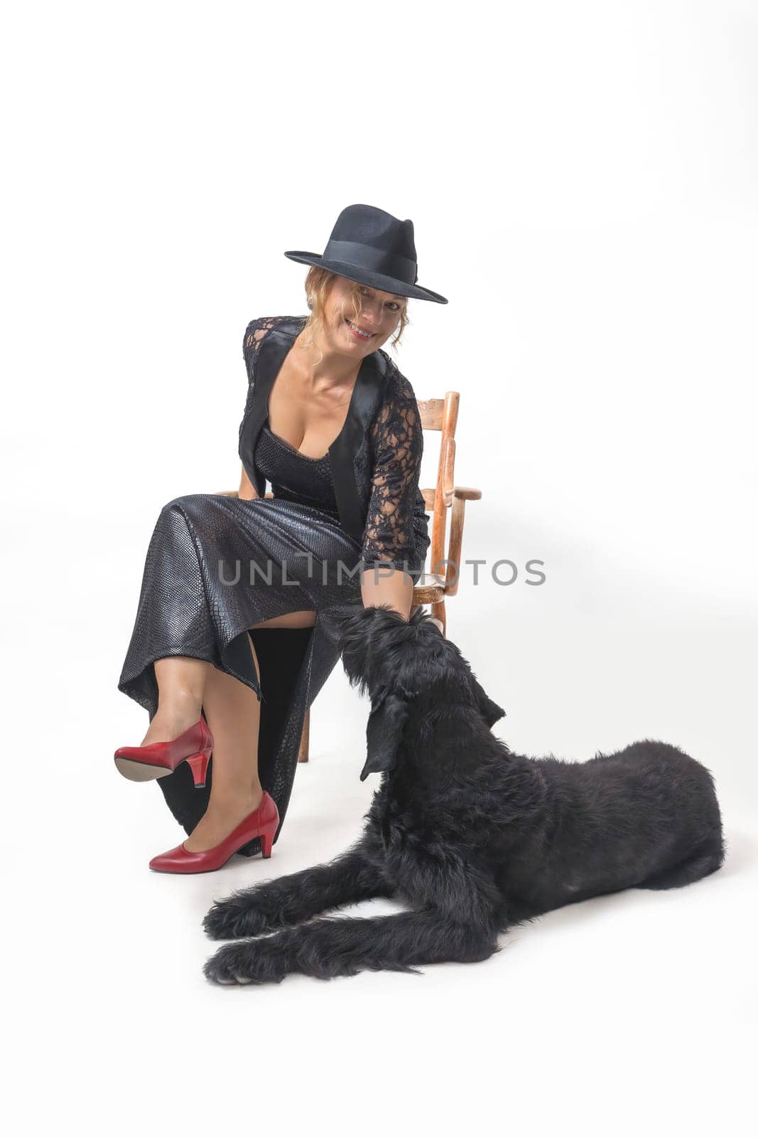 Middle aged woman is sitting on a chair in a studio. A Big Black Schnauzer dog is lying at her feet.