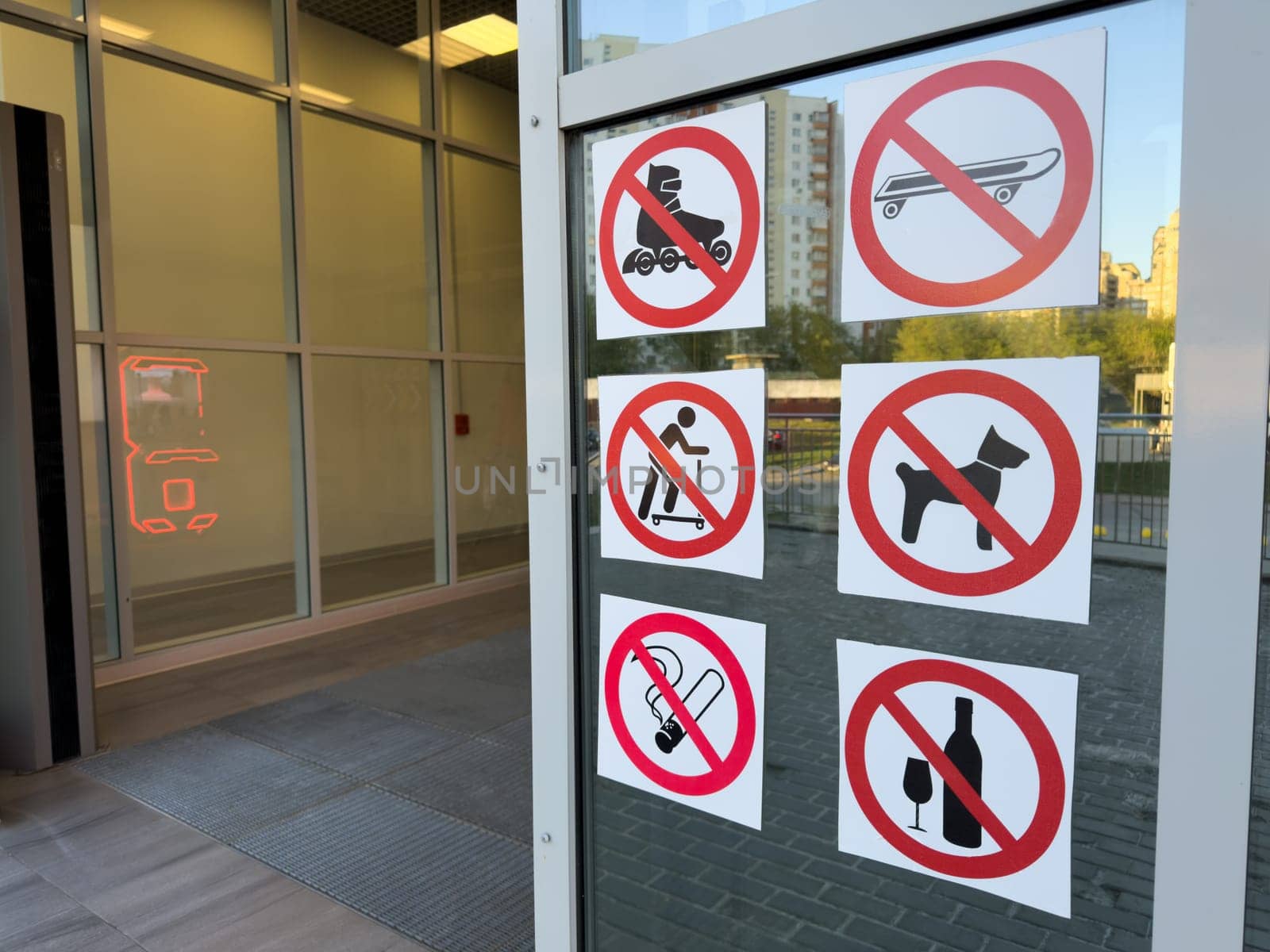 Set of bold prohibition signs on glass door showing banned items like dogs, alcohol, smoking, scooters and skateboards, emphasizing public order and facility regulations