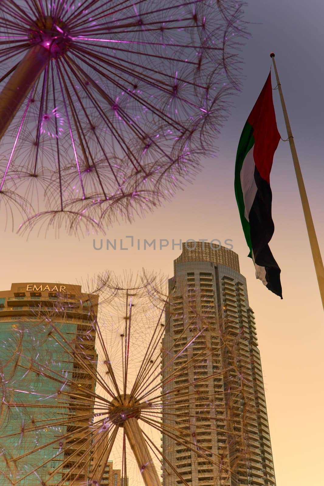UAE, Dubai, 11 December 2024: The famous Burj Khalifa skyscraper through the art object metal dandelions at dusk, Dubai's sights during the incredible sunset sky, skyscrapers illuminated. High quality photo
