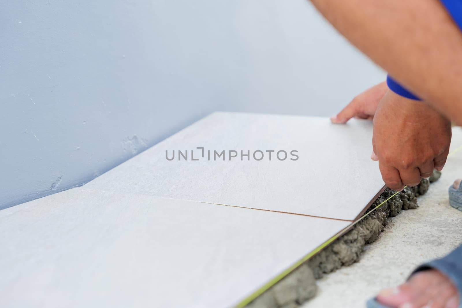 Hand carefully lays a white tile on gray mortar for home flooring, with another tile already set in position. The shot highlights the meticulous work of floor installation.