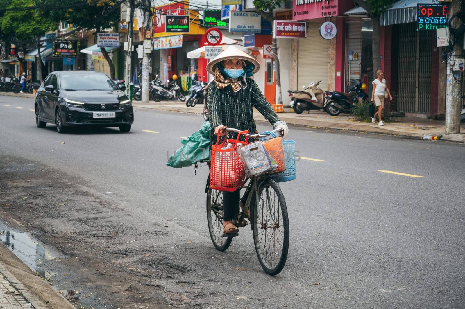 An elderly Vietnamese woman rides a bicycle on a road in Asia. Nha Trang, Vietnam - December 16, 2024