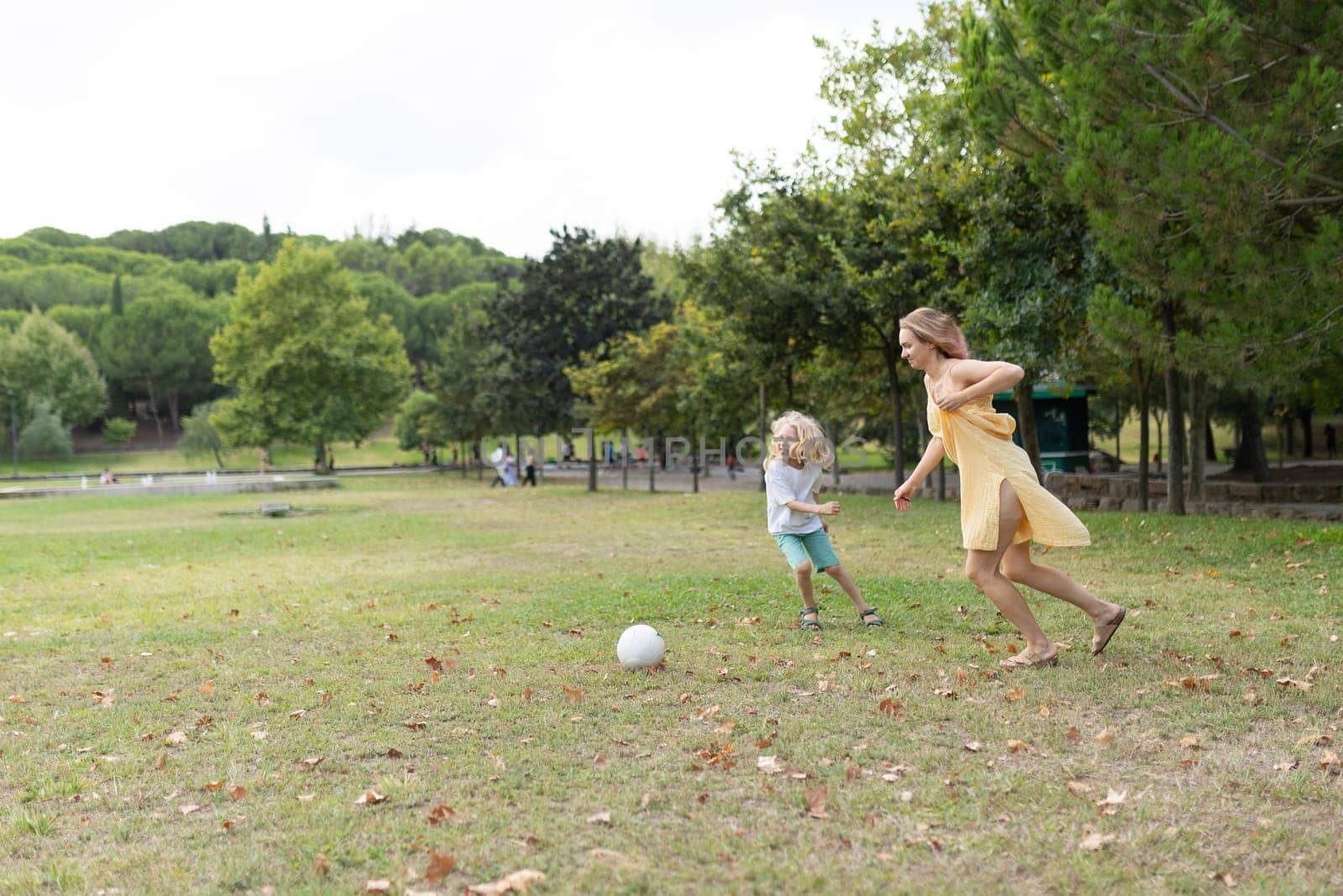 Happy family enjoying a sunny day at the park, playing soccer and running on the grass
