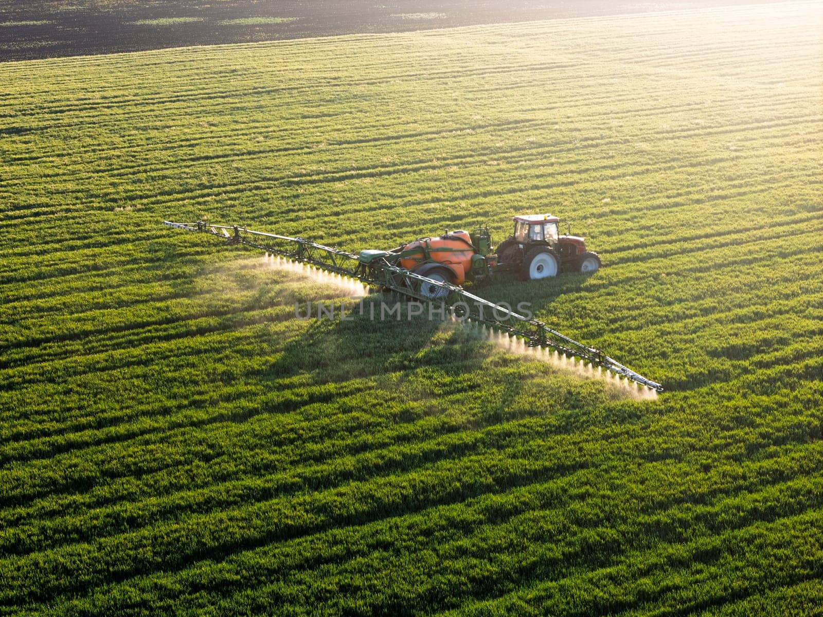 Aerial view of a modern tractor spraying crops with pesticides or fertilizers in a lush green field. Agricultural machinery in action represents sustainable farming, food production, and precision agriculture. Perfect for illustrating concepts in agribusiness, crop management, and rural technology