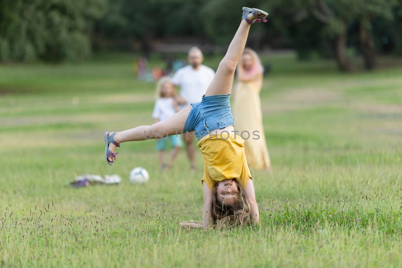 Girl doing a cartwheel in a park while her family watches in the background, enjoying a sunny day outdoors