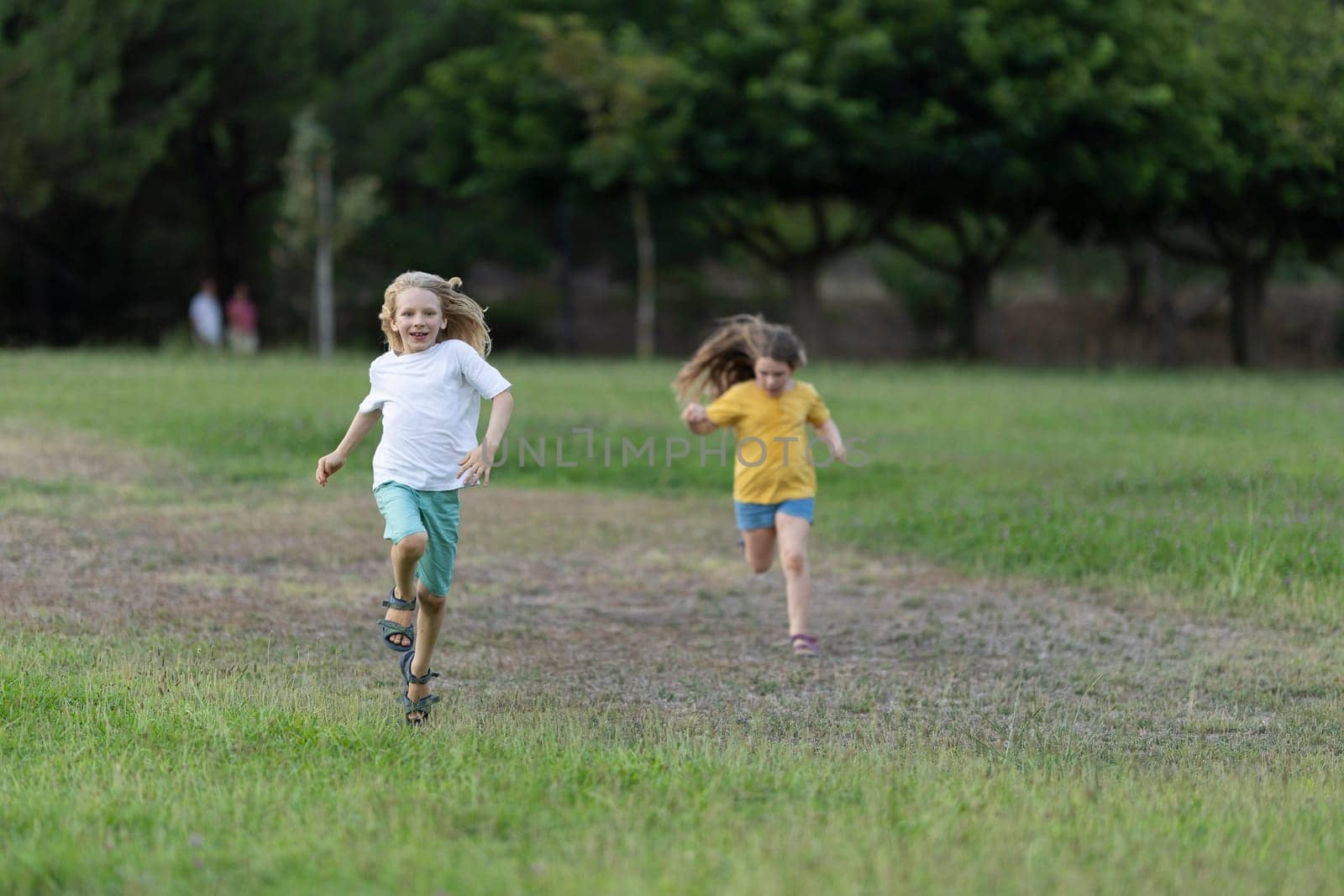 Two children running happily on the grass in a park, enjoying a sunny day outdoors