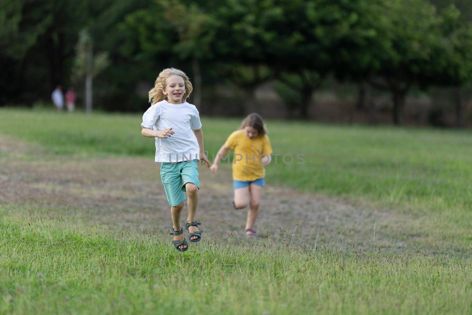 Two joyful kids running on grass in a park, enjoying summer holidays