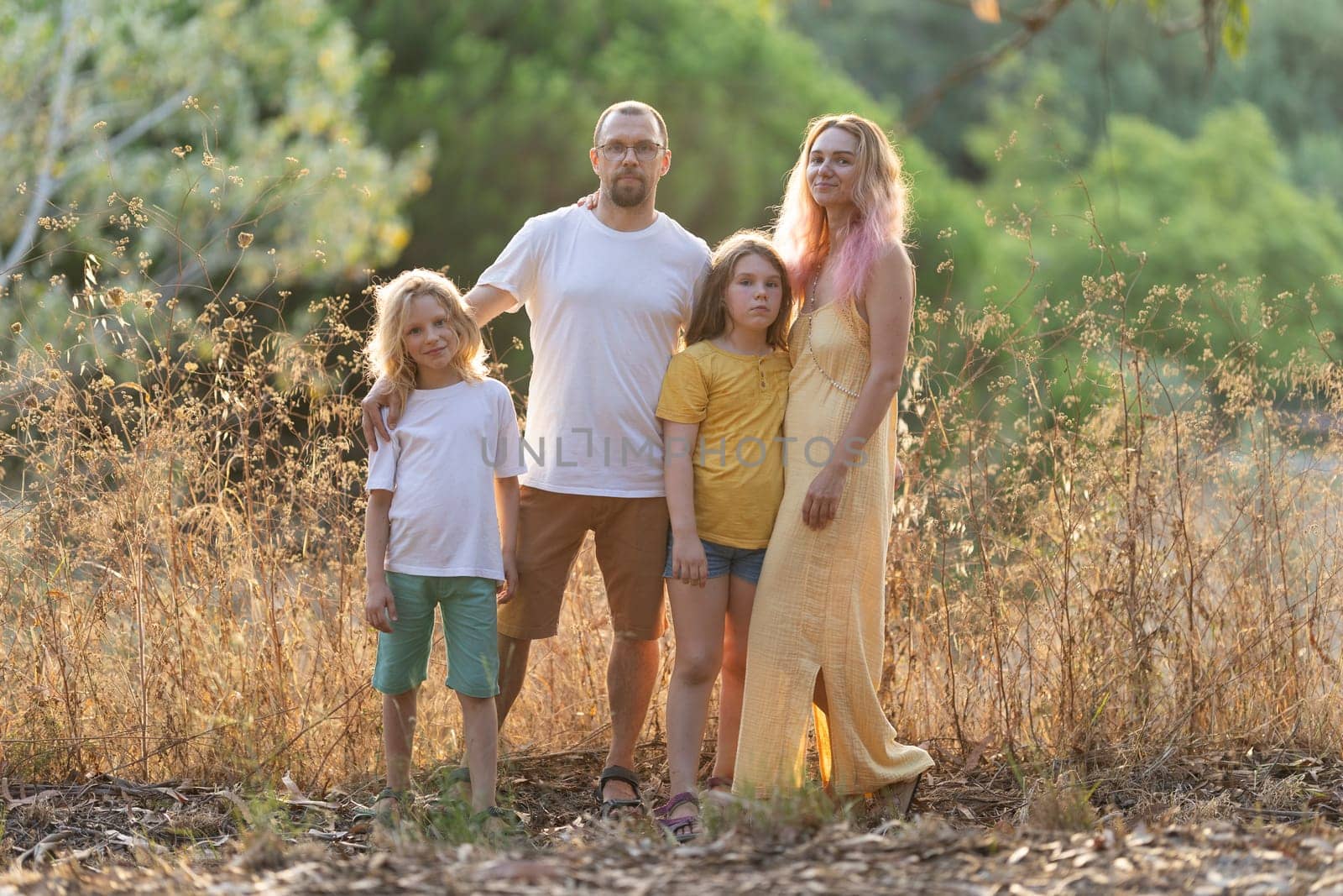 Family with two children posing together outdoors in tall grass at golden hour