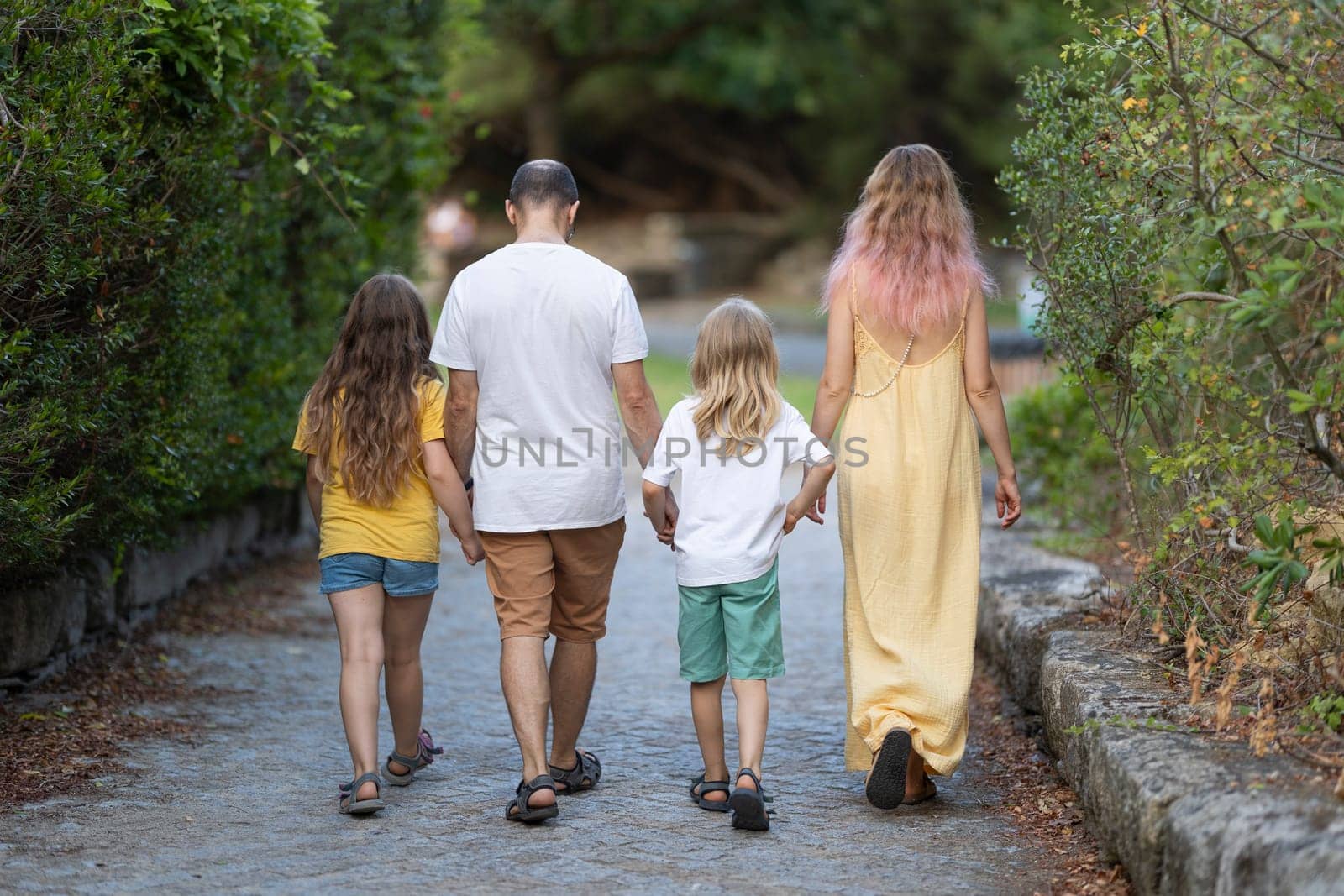 Family of four walking away on a path in a park, holding hands