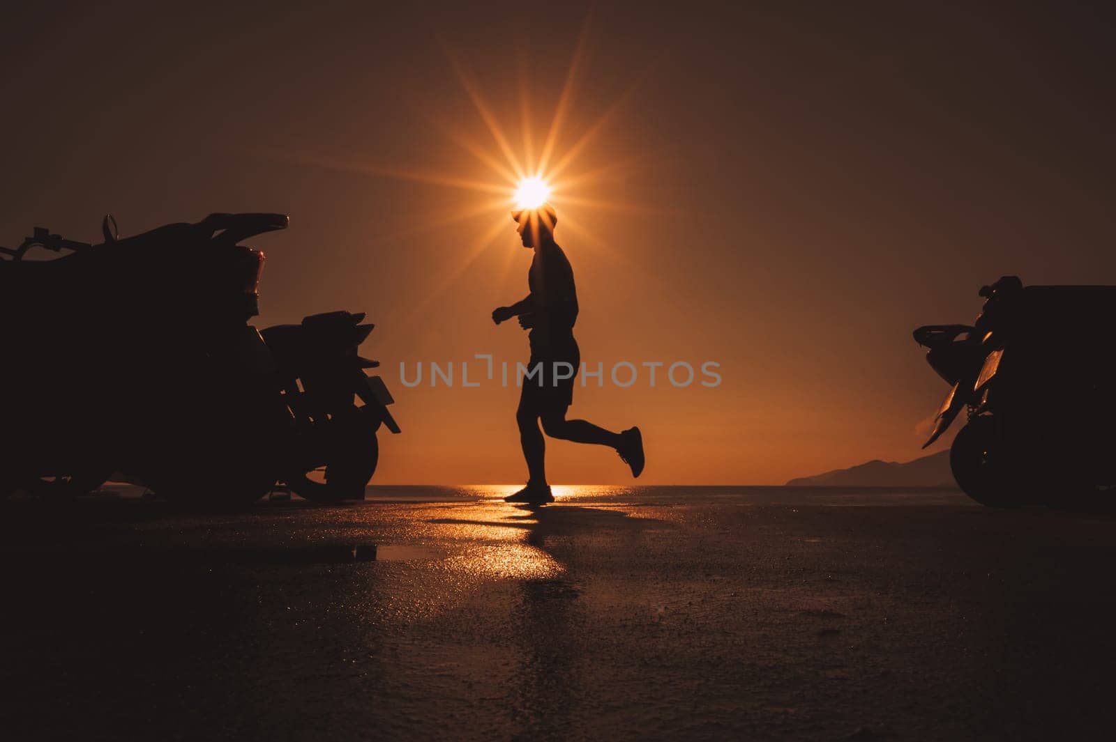 silhouette of a male athlete running along the sea embankment at dawn in the morning