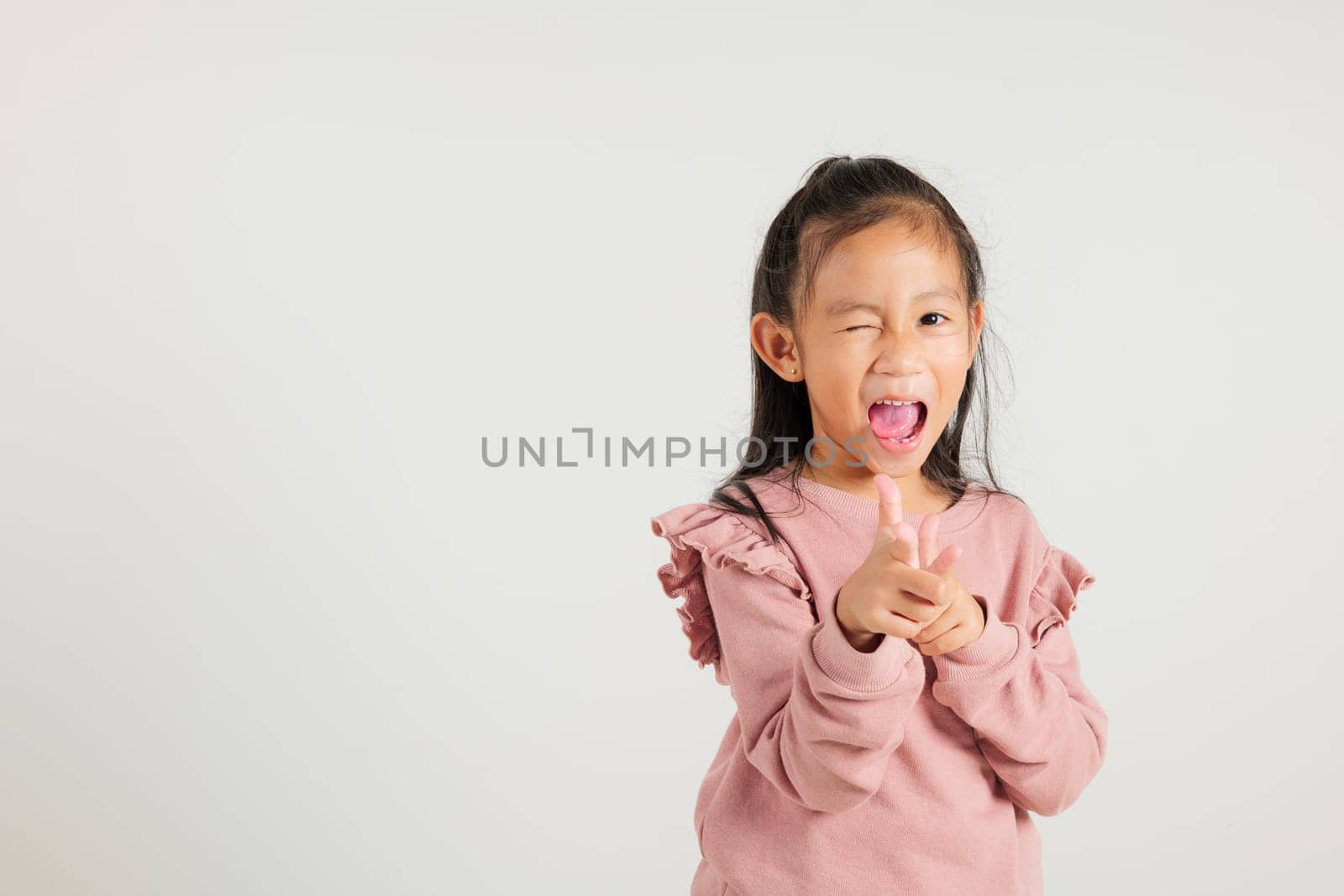 Cheerful Asian young kid girl excitedly makes two gun finger gesture to the camera with a friendly and cheeky expression. Isolated on white background, kindergarten child exudes positivity and joy