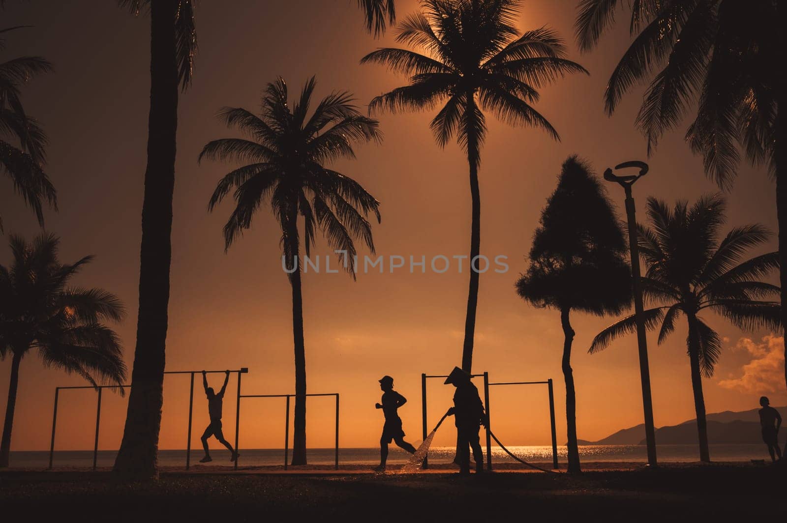 silhouettes of people on the embankment with palm trees by the sea at sunrise on a summer morning